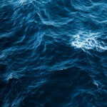 "A calming aerial view of the deep blue ocean, with gentle waves creating subtle ripples across the water's surface, perfect for a serene mobile wallpaper