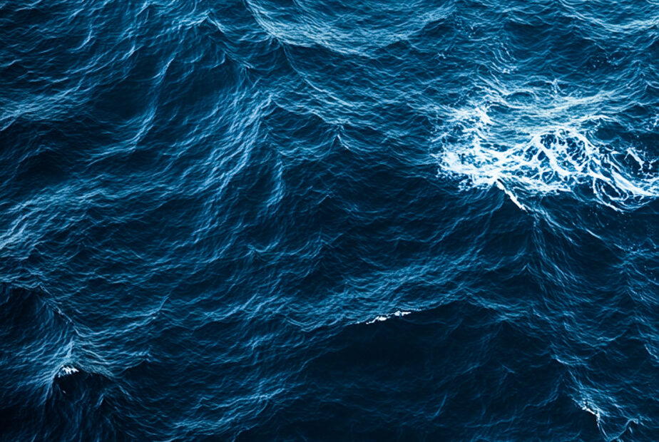 "A calming aerial view of the deep blue ocean, with gentle waves creating subtle ripples across the water's surface, perfect for a serene mobile wallpaper